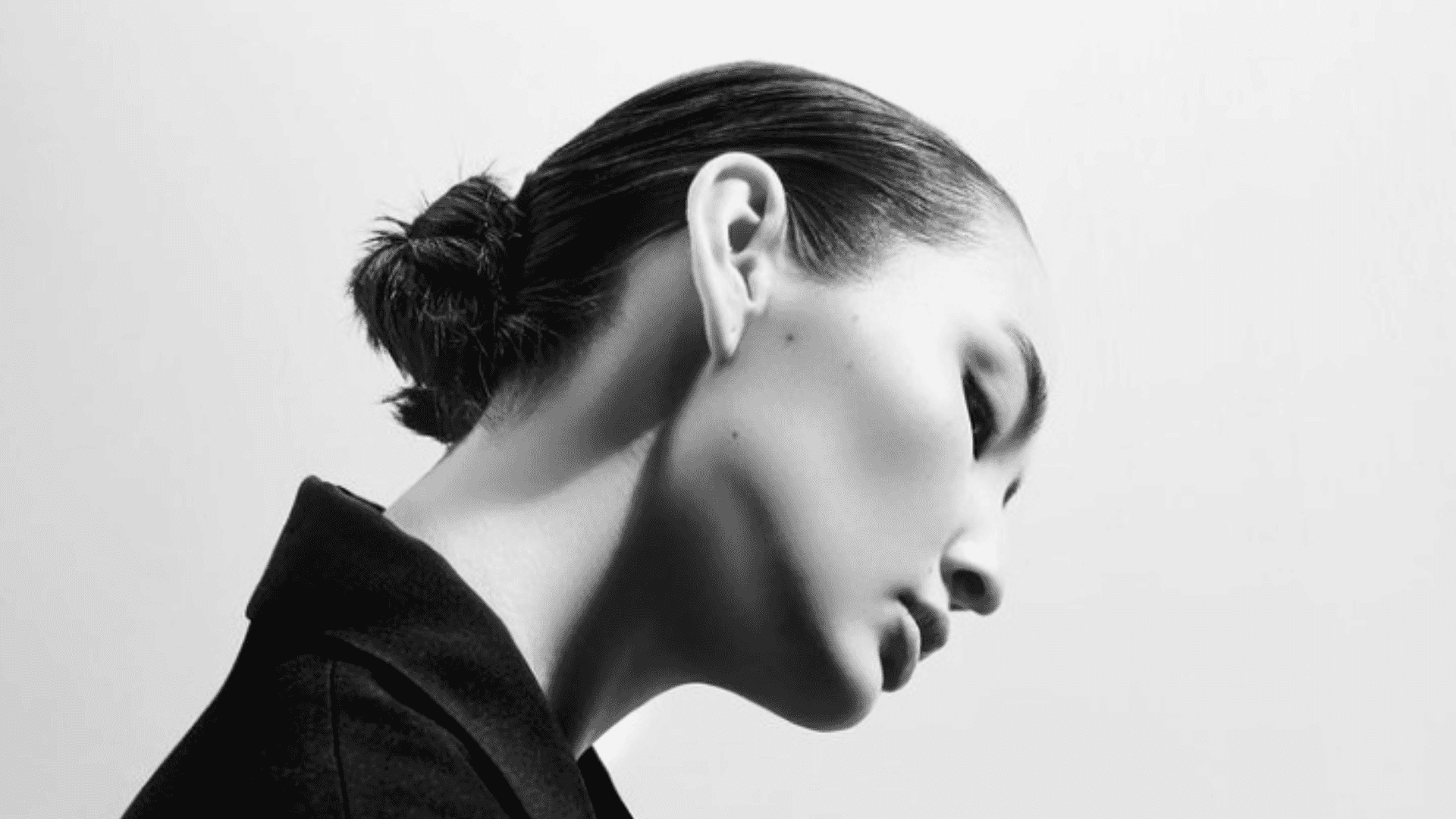 Profile of a woman with slicked-back hair in monochrome, looking down against a plain background.